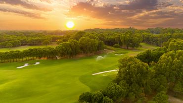 Sunset over a lush green golf course surrounded by trees.