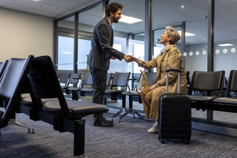 Medium shot of a female solo traveller sitting down in an airport departure lounge. A male staff member is standing up beside her while shaking her hand. They are both looking at each other and smiling. 

Videos are available similar to this scenario.