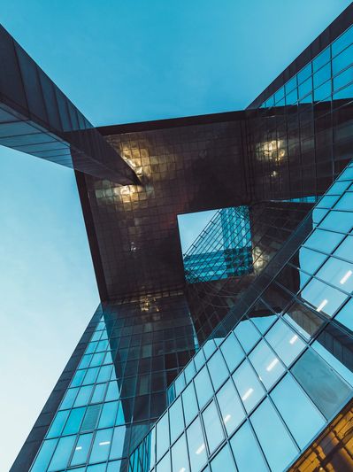 Looking up at a modern glass skyscraper with reflective blue windows and geometric design.
