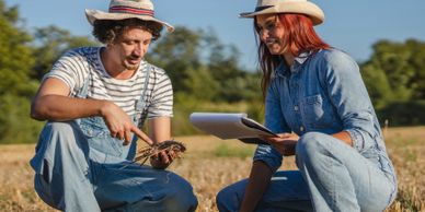 Two farmers examining soil and taking notes in a field.