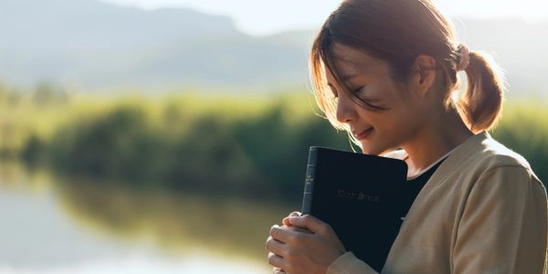 Woman holding a Bible outdoors with a serene smile.