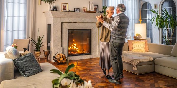 Elderly couple dancing warmly by a cozy fireplace in a beautifully decorated living room.