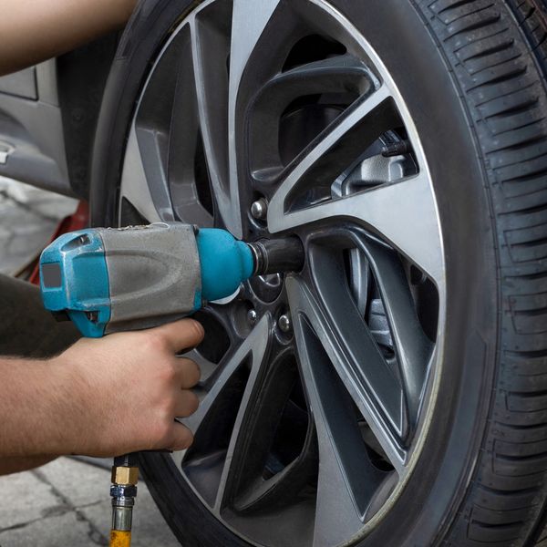 Person using an impact wrench to tighten car wheel nuts.