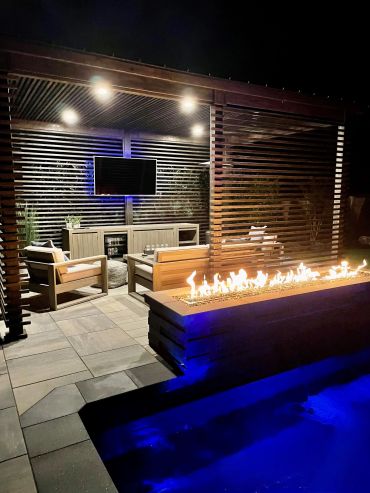 Modern outdoor lounge with fire feature and pool lighting at night.