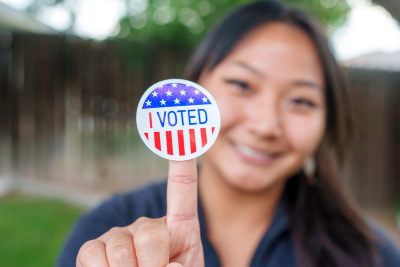 Young Mixed-Race Vietnamese Filipino Woman Happily Displaying Her I Voted Sticker Outside in a Yard After She Has Done Her Civic Duty By Voting in an Election