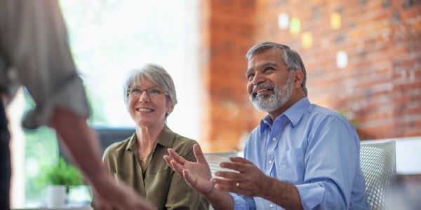 Two senior coworkers engaged in a discussion with a standing colleague.