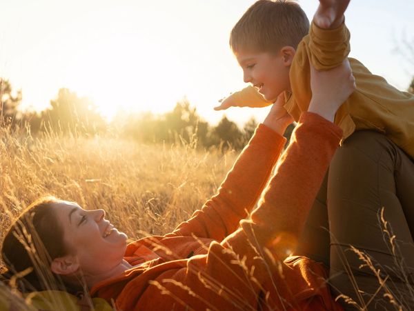 Mother and child playing joyfully in a sunlit field.
