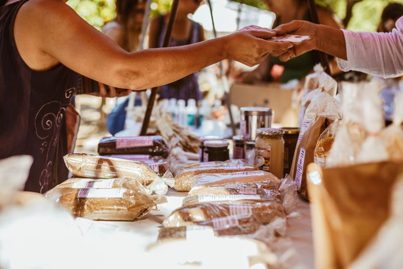 Hands exchanging money at an outdoor market stall with packaged goods.