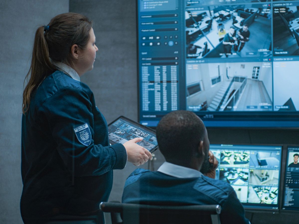 Two security personnel monitoring surveillance footage in a control room.