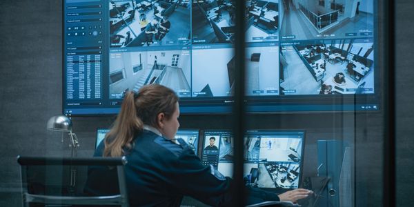 Security personnel monitoring multiple surveillance camera feeds in a control room.