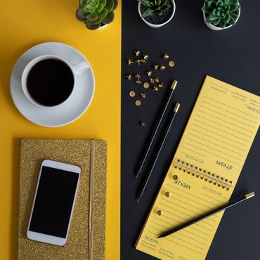 Organized desk with coffee, phone, notebook, and plants on contrasting yellow and black background.