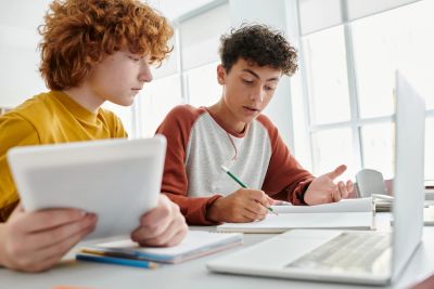 Two students collaborating on homework with a tablet and notebook.