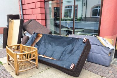 Discarded old furniture piled on a sidewalk outside a building.