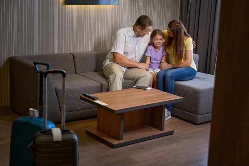 Hotel guests with their little daughter sit on a cozy sofa, parents hug the baby