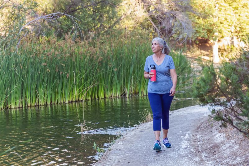 Woman walking on outdoor footpath holding reusable water bottle