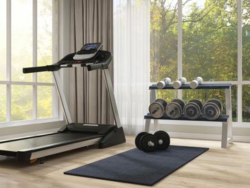 A modern home gym with a treadmill, dumbbells, and a yoga mat by large windows.