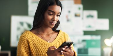 Woman in yellow sweater using smartphone indoors.