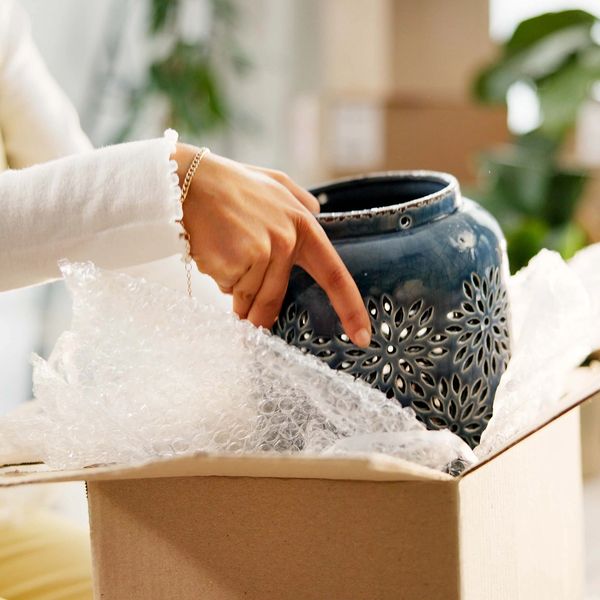 Person unpacking a decorative ceramic vase from a cardboard box.
