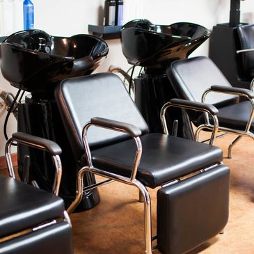 Black salon chairs lined up in a hair salon beside wash basins.