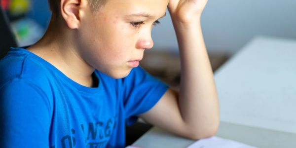 A boy in a blue shirt concentrating on his homework at a desk.