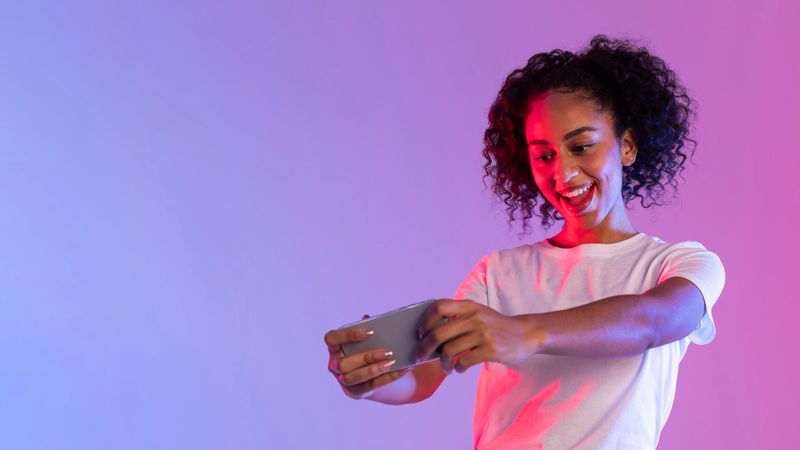 Excited woman focusing on her smartphone while playing a game against a neon pink and purple background