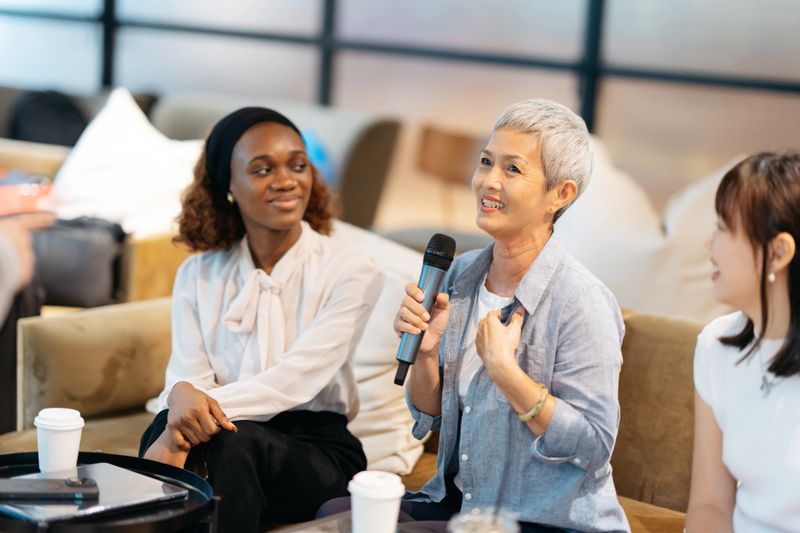 Mature Asian businesswoman asks someone on a panel of experts a question during a business conference or seminar.