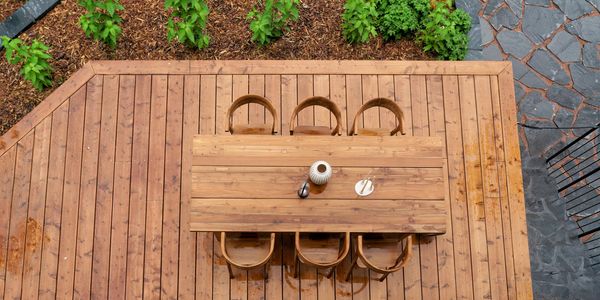 Top view of a wooden outdoor dining set on a deck with plants nearby.