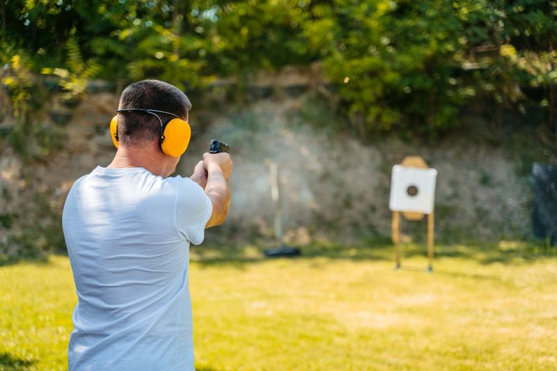 Mid-adult man shooting a target with a handgun in an outdoor shooting range.