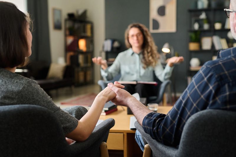 Counseling session showing couple holding hands while therapist gesturing in modern office setting focusing on communication and support