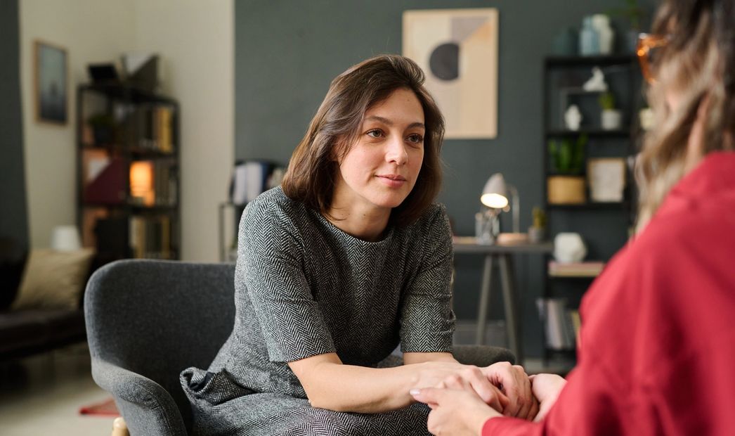 A woman attentively listens and holds another person's hands in a cozy room.