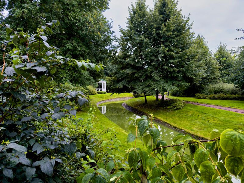 A peaceful garden scene featuring a charming white gazebo reflecting in a tranquil pond, surrounded by lush greenery. The serene atmosphere is enhanced by the soft lighting and natural beauty, making this image ideal for projects focused on outdoor spaces, relaxation, and scenic landscapes
