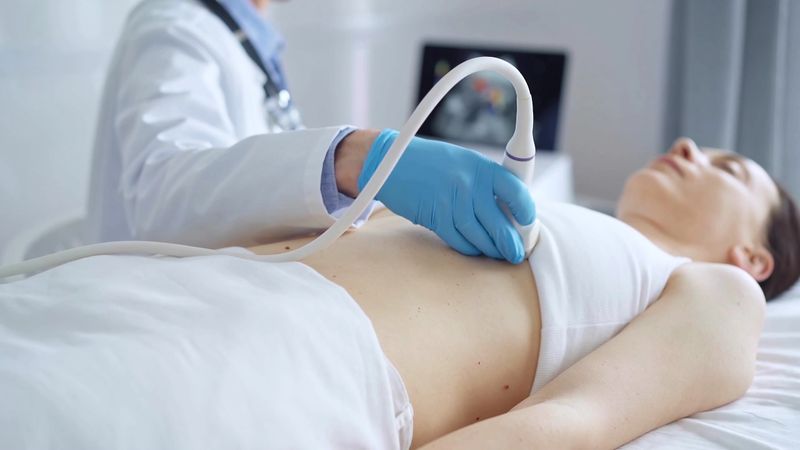 Doctor man, wearing blue medical gloves, is using ultrasound equipment on the breast of a female patient lying down for a medical cardiology examination. Medicine concept.