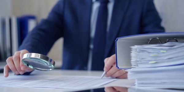 Person reviewing documents with magnifying glass in office.