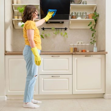Woman in yellow gloves cleaning kitchen hood with a cloth.