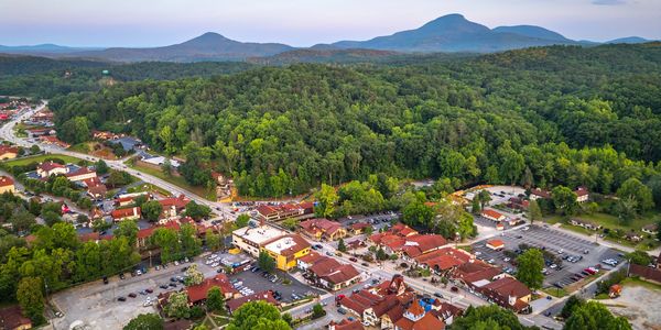 A small town nestled near lush green forests and mountains under a clear sky.