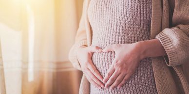 Pregnant woman forming a heart shape with her hands on her belly.
