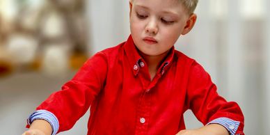 Young boy in a red shirt coloring and drawing at a table.