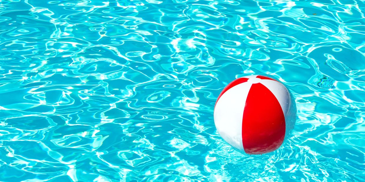 Red and white beach ball floating on clear blue pool water.