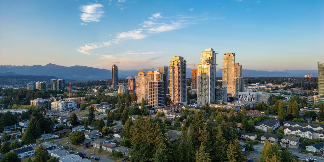 City skyline with tall buildings and greenery under a clear blue sky at sunset.