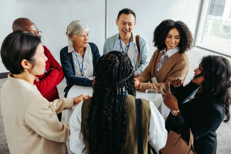 Multiethnic diverse business people of various ages socializing and networking around a table in an office environment. Professional interaction and collaboration.