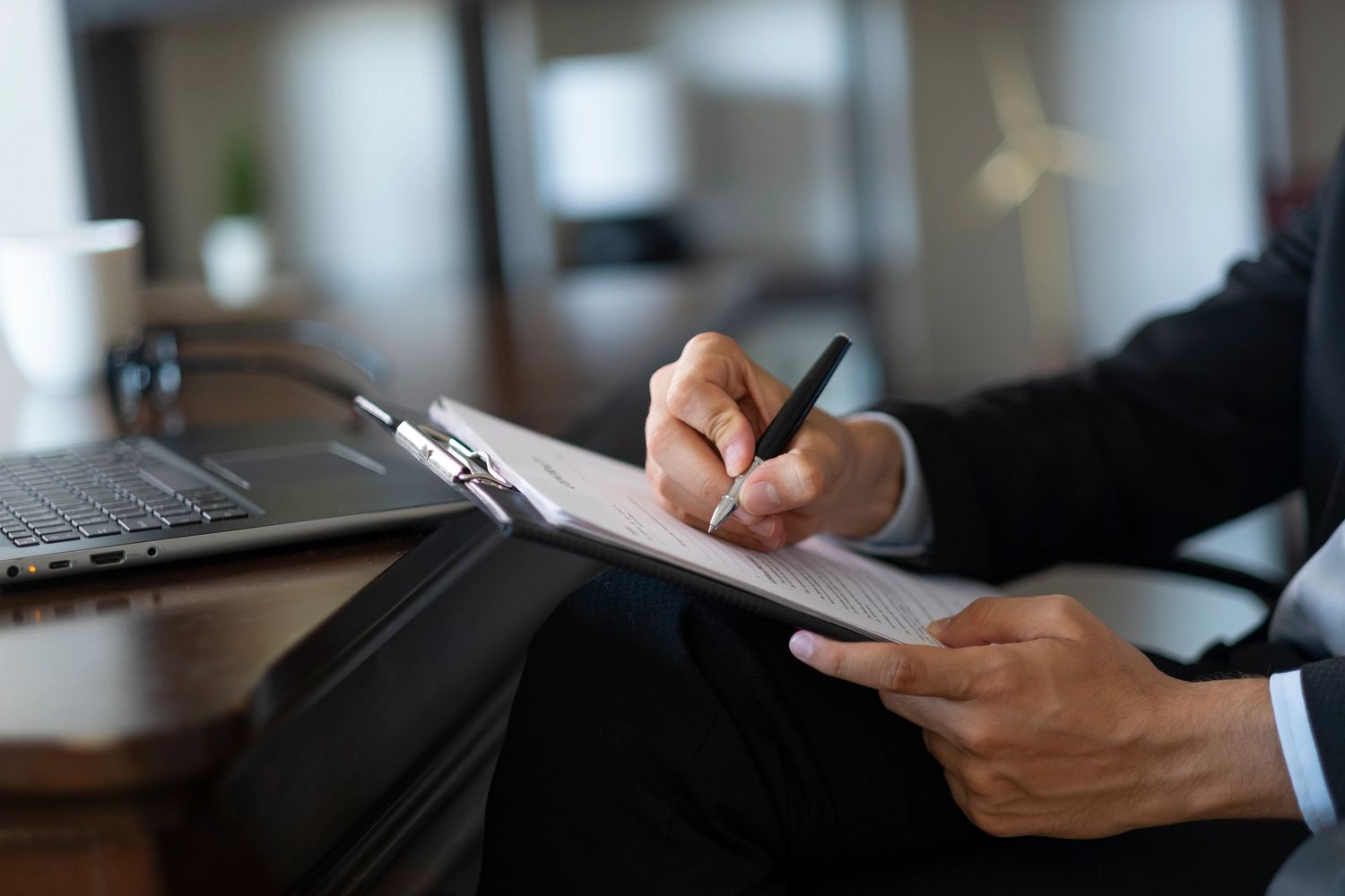 Person in business attire writing on a clipboard at a desk.
