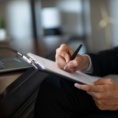 Person writing on a clipboard next to a laptop.