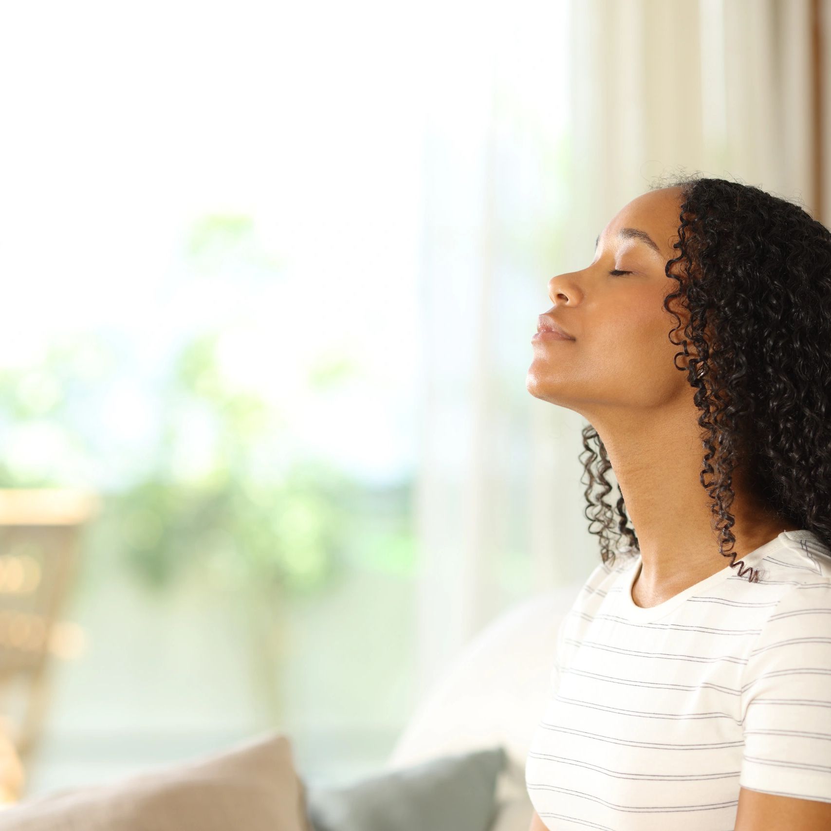 Woman by a sunny window taking a calm, deep breath