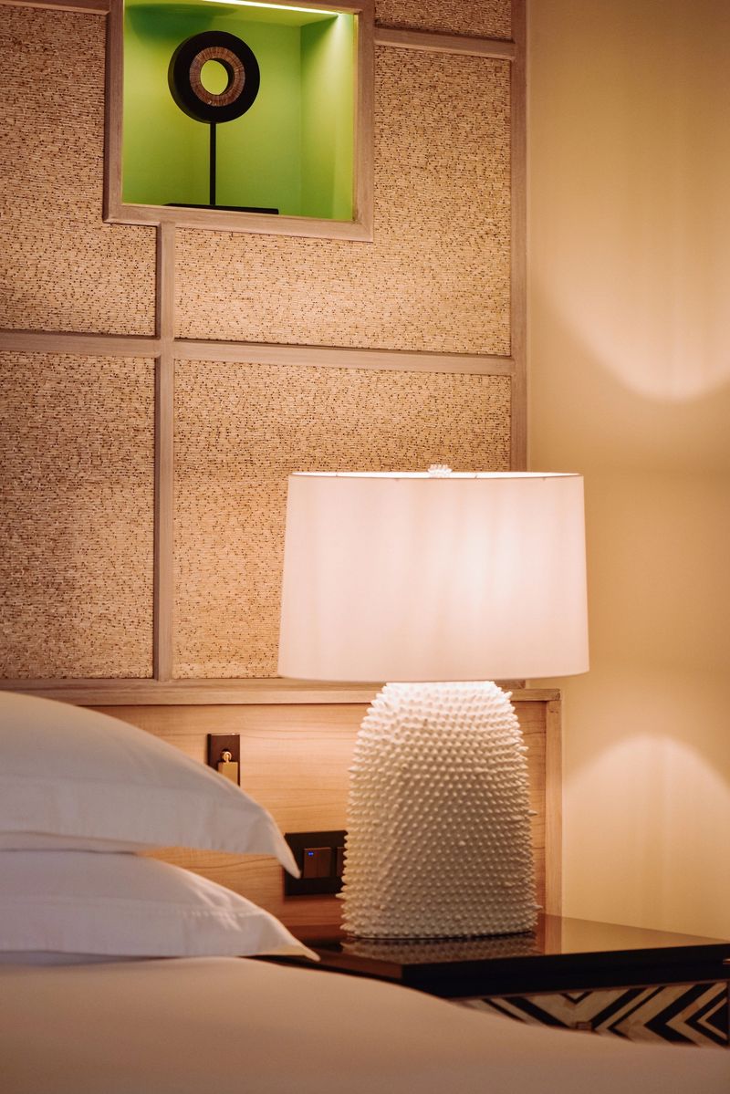 cozy bedroom nightstand with warm light lamp shade in luxury hotel room with white linen bedsheets and fluffed up pillows