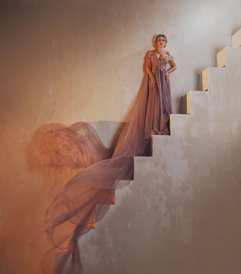 Fairy lady queen fashion model standing on steps staircase old style, beauty Princess girl in royal lush long fabric train skirt gown purple dress fly. Sexy Fantasy woman raises stairs art photo.