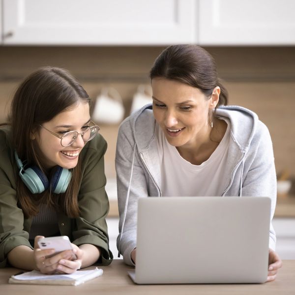 Two women happily working together on a laptop in a kitchen.
