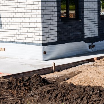 Corner of a brick house under construction with fresh concrete and soil around.