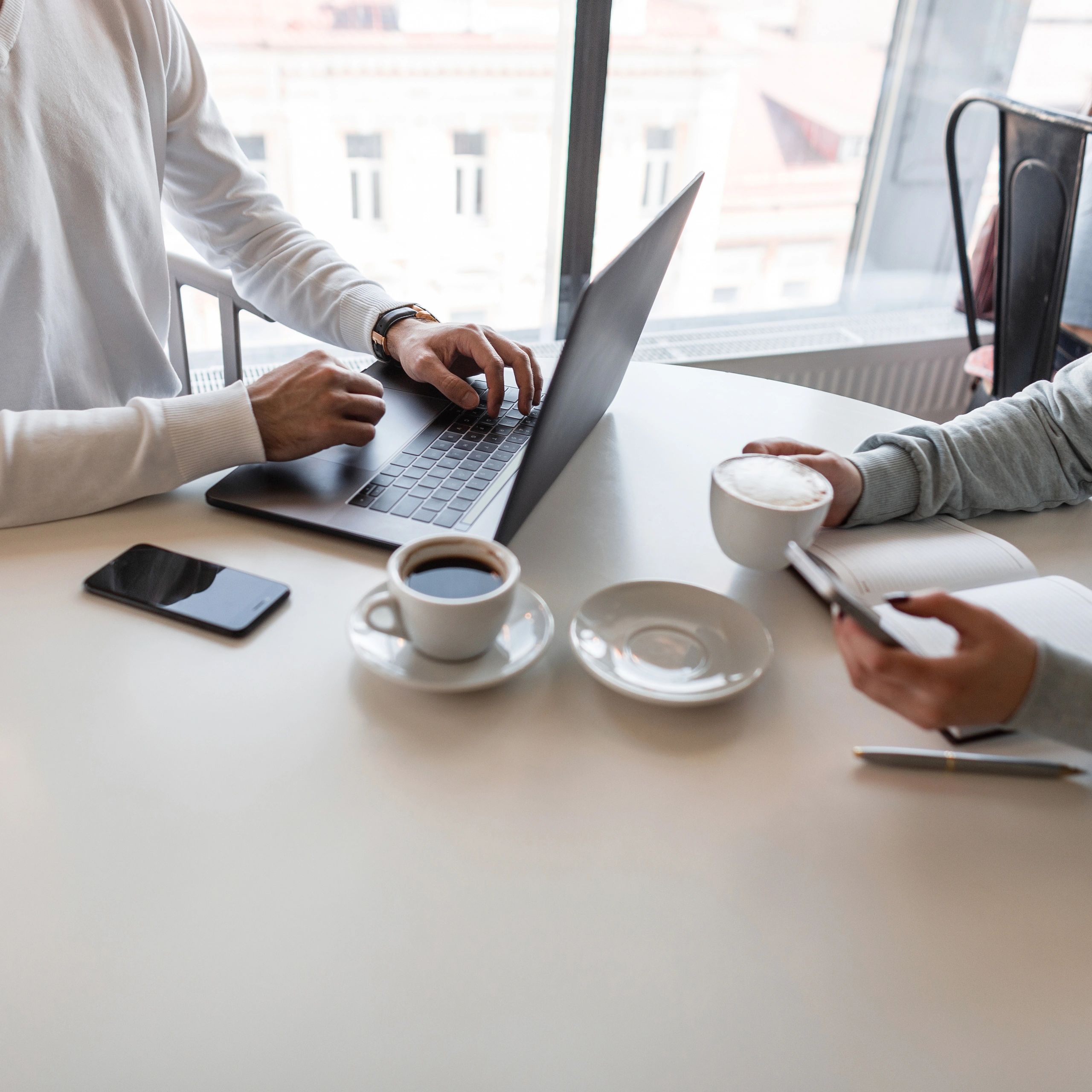 Two people working together with coffee and laptop at a bright table.