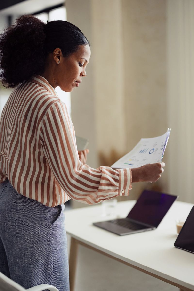 A businesswoman carefully examines financial documents in a contemporary office, demonstrating focus and professionalism. Laptops and business charts enhance the corporate atmosphere.