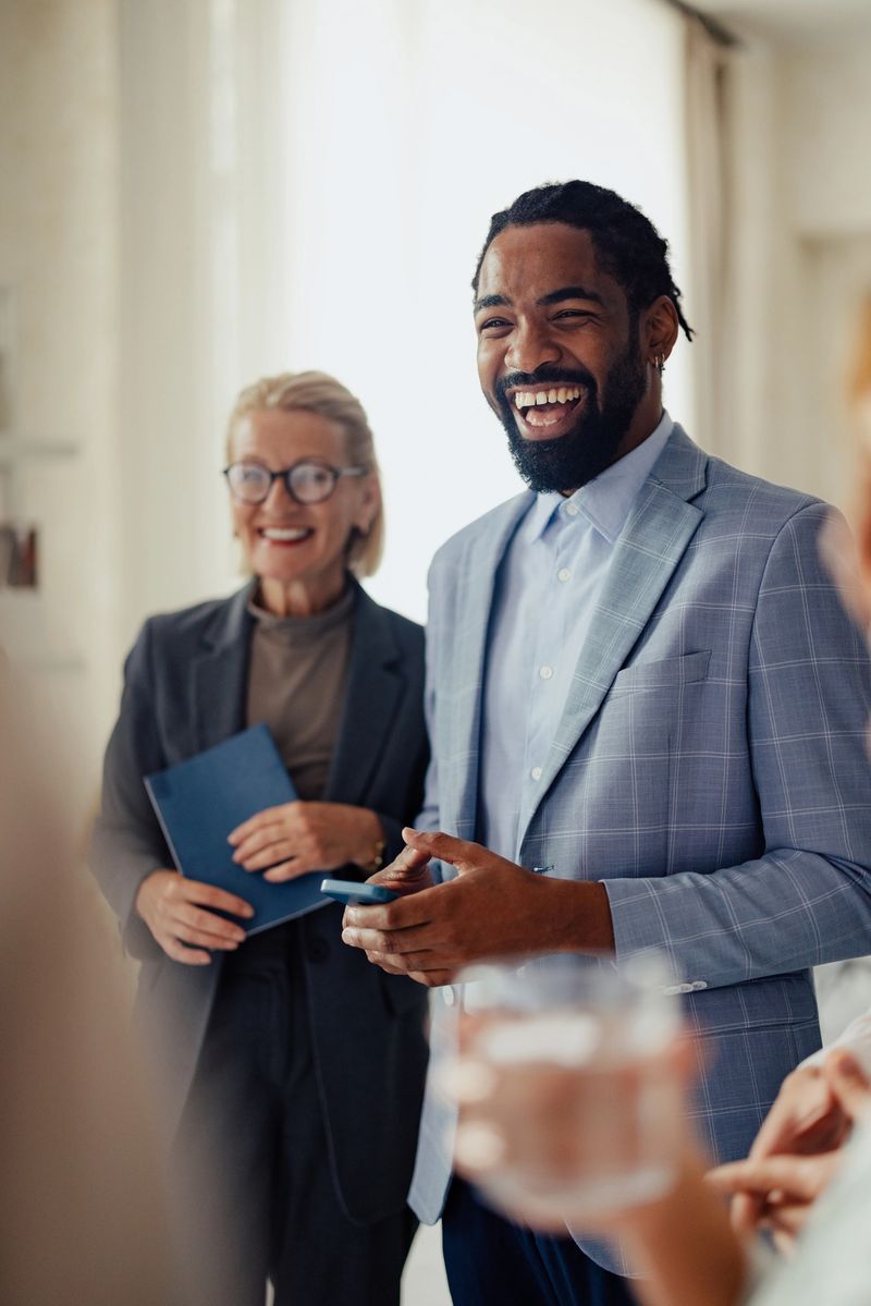 A group of diverse professionals smiling and interacting during a business meeting in a modern office setting. The atmosphere is collaborative and positive, showcasing teamwork and success.